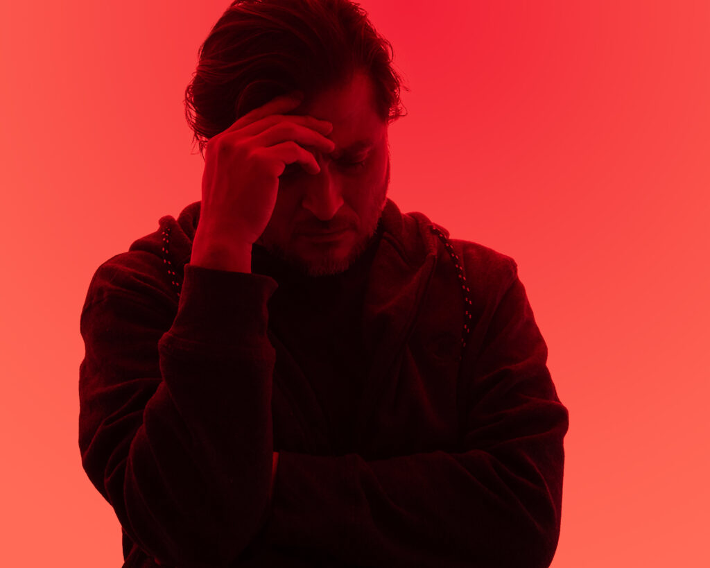 Man with a headache on red backdrop.